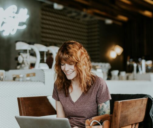 woman sitting on brown wooden chair while using silver laptop computer in room